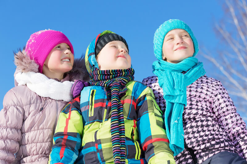 three children wrapped up in hats, scarves and winter coats