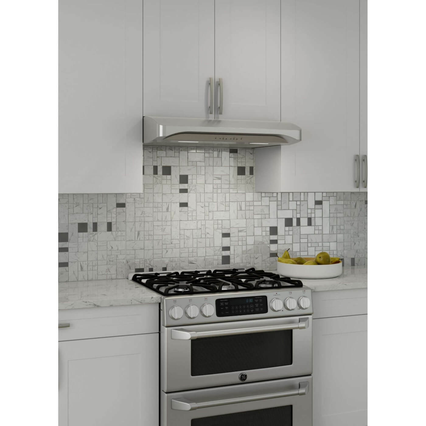 Contemporary kitchen design showcasing a Broan Elite Alta III Series stainless steel convertible under-cabinet range hood, with a geometric tile backsplash and a gas stove. A white bowl of green pears on the countertop adds a splash of color to the monochrome palette