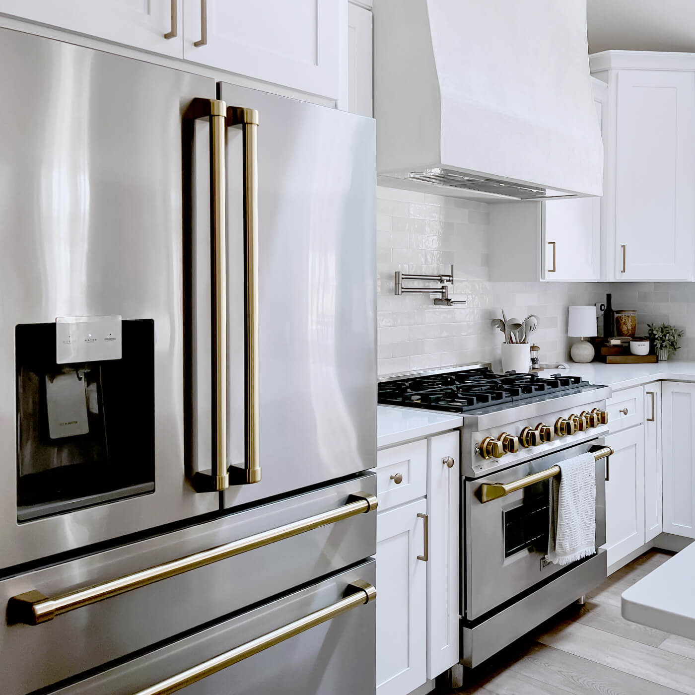 A sleek and modern kitchen interior showcasing a ZLINE 36-inch refrigerator with brass handles alongside a coordinating ZLINE gas range with brass burners, set against white cabinetry and subway tile backsplash, embodying luxury and functionality