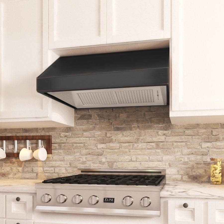 Classic kitchen aesthetic featuring a ZLINE Designer Series oil-rubbed bronze under cabinet range hood above a professional gas stove, set against a textured stone backsplash, with white cabinetry providing a bright contrast.