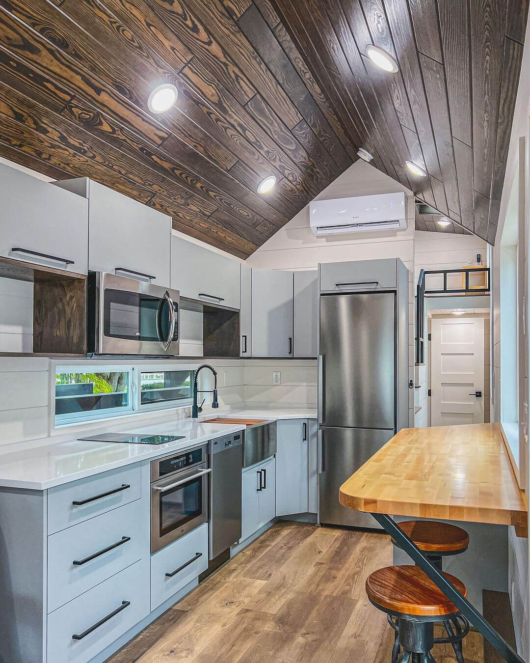 Summit Appliances Lifestyle - white kitchen in a tiny home with stainless steel appliances light hardwood floors and back hardware on cabinetry 