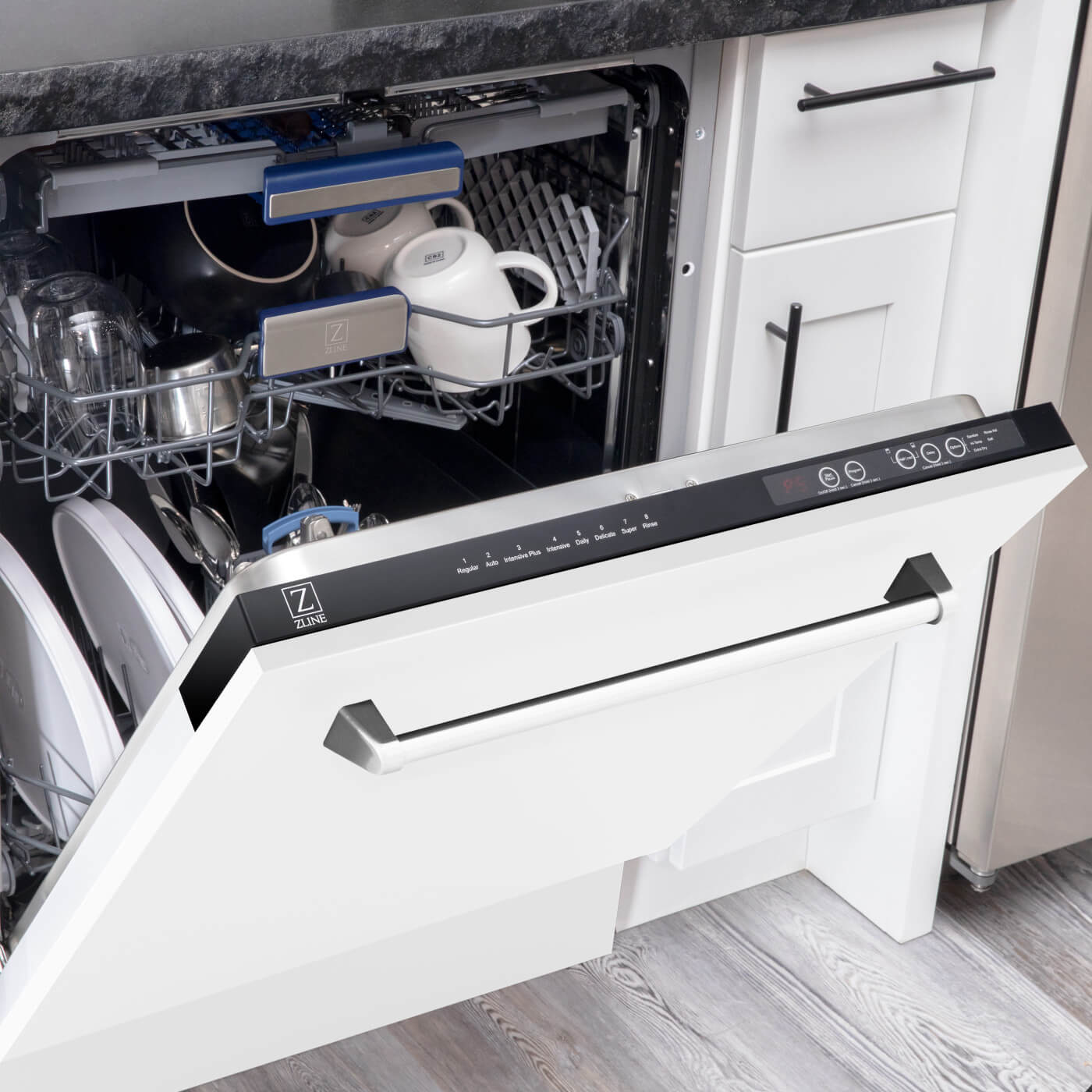 An open ZLINE matte white dishwasher, model DWV-WM-24, revealing a loaded interior with dishes and cups, integrated seamlessly into a kitchen with white cabinets and dark handles, combining practicality with a sleek, modern design.