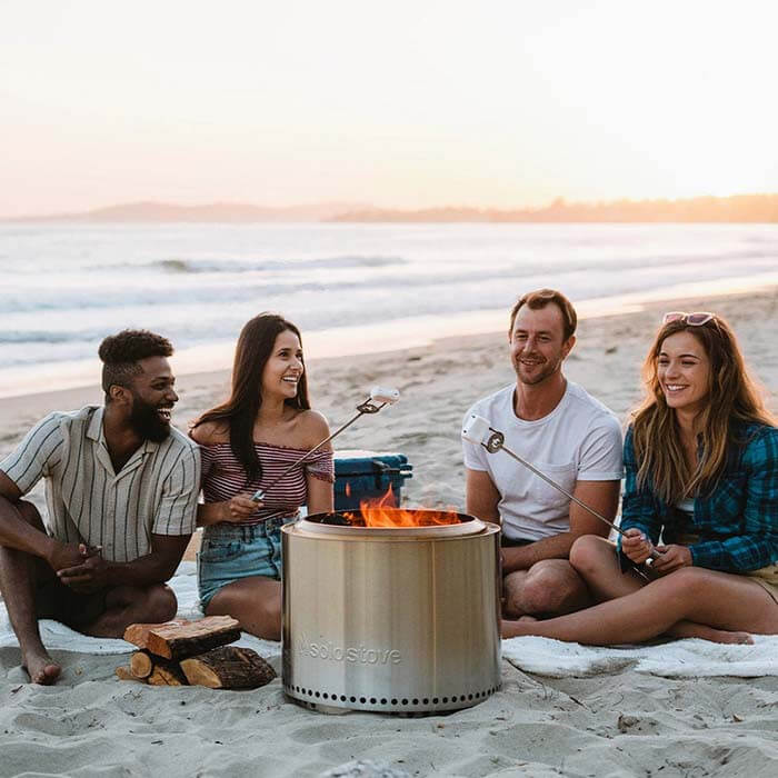 Group roasting marshmallows on a beach with a smokeless fire pit.