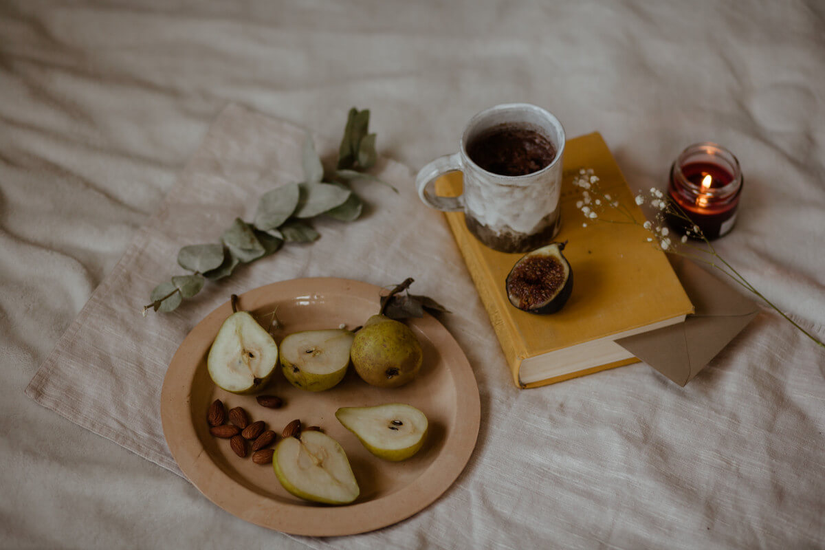 plate of pears next to a book and a candle