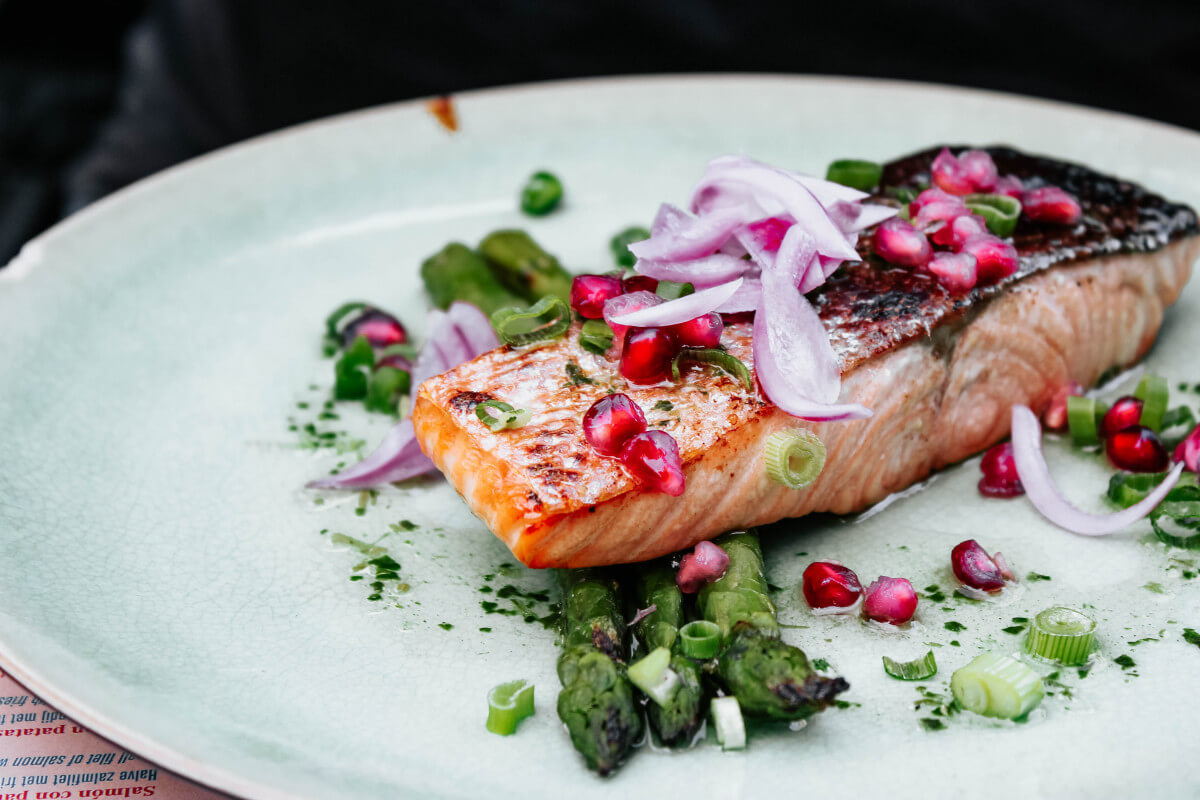 salmon filet on a white plate with asparagus and red onion