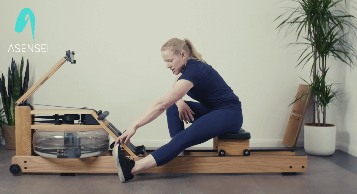 Clare Holman does a hamstring stretch, sitting on a WaterRower rowing machine
