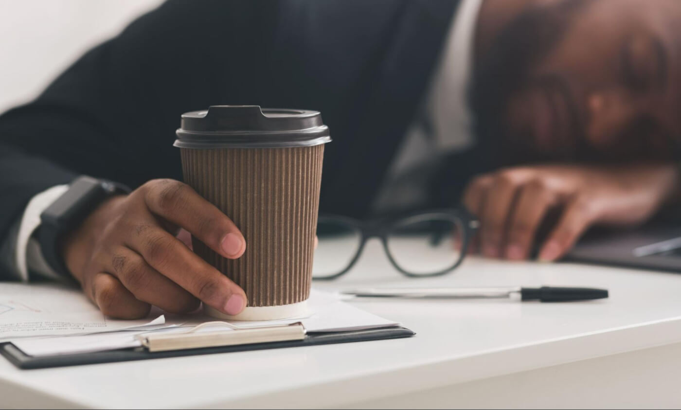 Cup of coffee held by a businessman sleeping on his desk