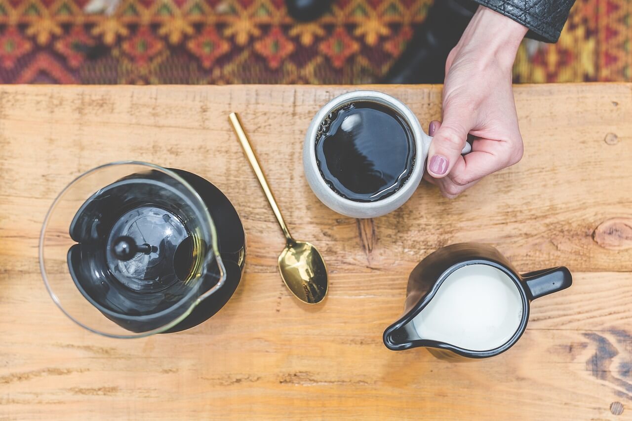 Coffee cup with a gold spoon, milk pitcher, and coffee pot nearby