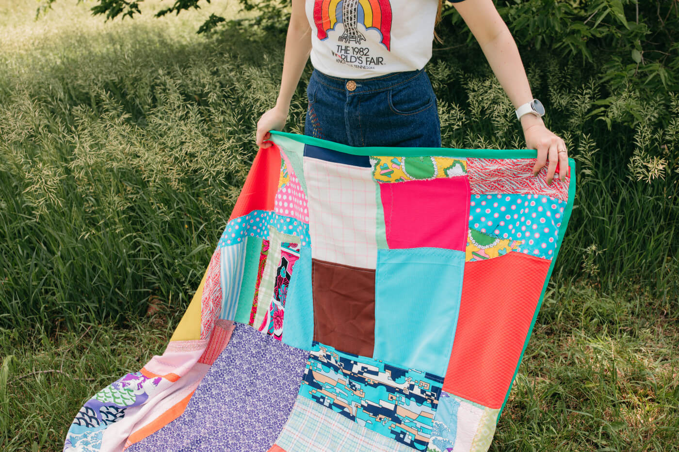 A white woman spreads a patchwork blanket over the grass.