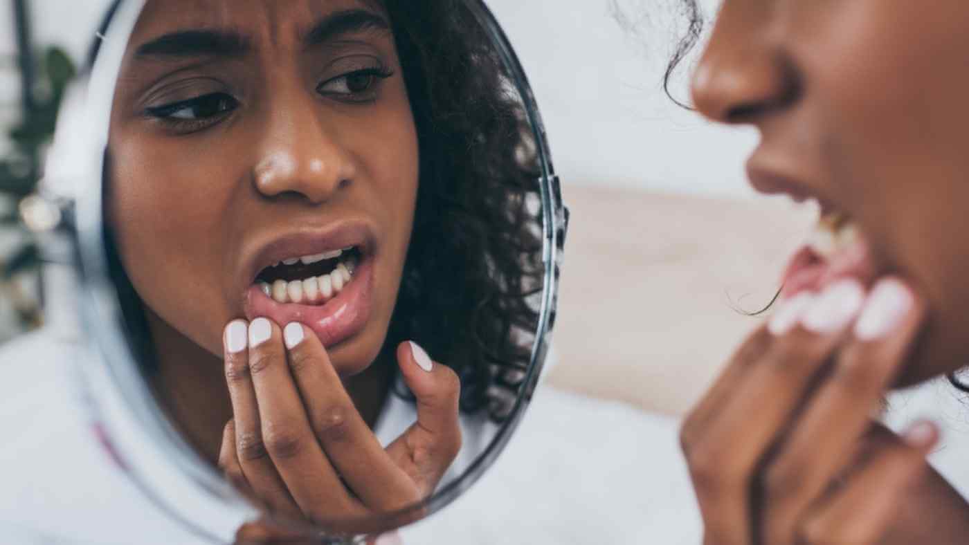 young woman looking in mirror; root canal tooth pain