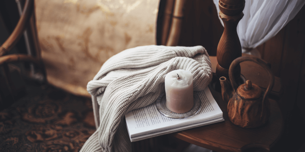 A sweater, unlit candle, book, and tea kettle on top of a chair