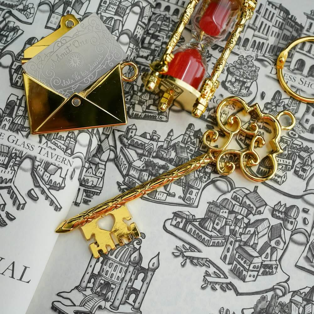 A key to caraval including two charms: an hourglass game piece with red sand and an envelope with the engraved ticket inside