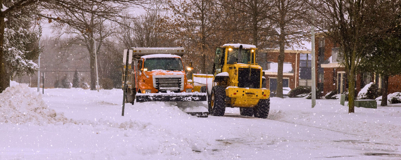 Two snowplows plowing a residential street during a snowstorm.
