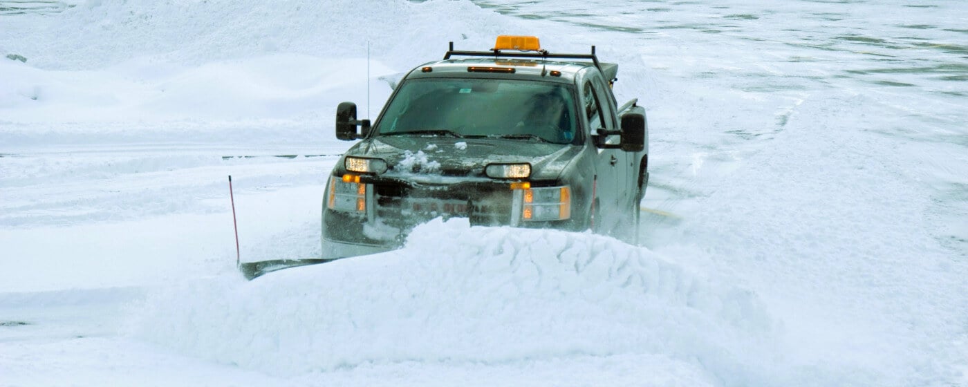 GMC Pickup truck fitted with a snowplow pushing large snow bank in a snowy parking lot.