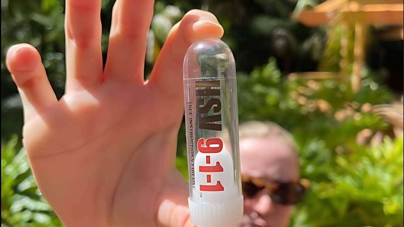 Picture of a person holding a clear tube, its the packaging for HSV 911. they are outside and there are trees inthe background