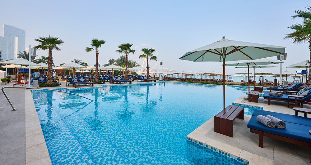 Rixos Premium Dubai's bright blue pool surrounded by sunbeds in the sun
