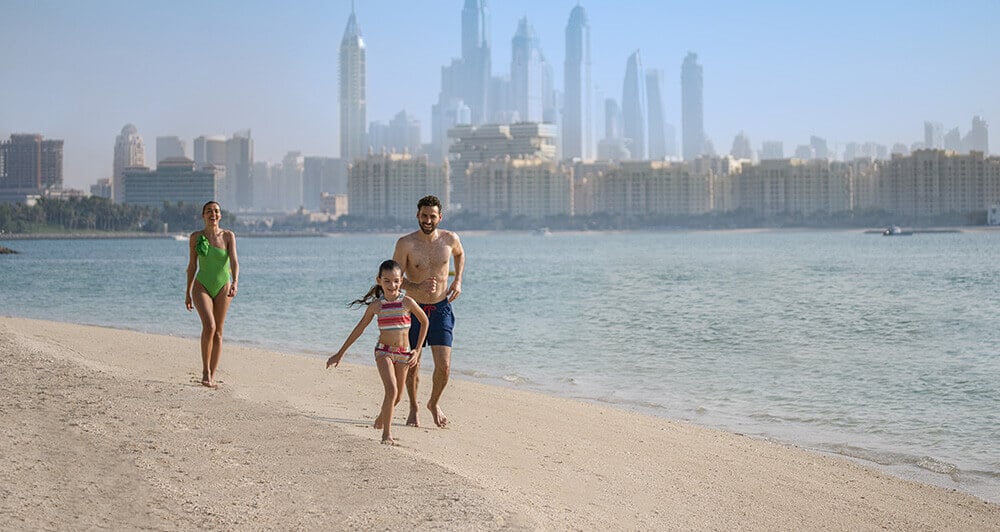 A family playing together and running on the beach at Rixos The Palm