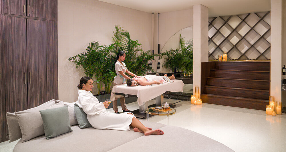 A couple getting a massage at the spa at Rixos The Palm. The lady is sat on the bed in a dressing gown while the man is getting a massage on a table